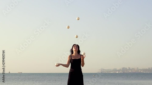 beautiful young woman juggles balls on the sea beach. Evening sun
