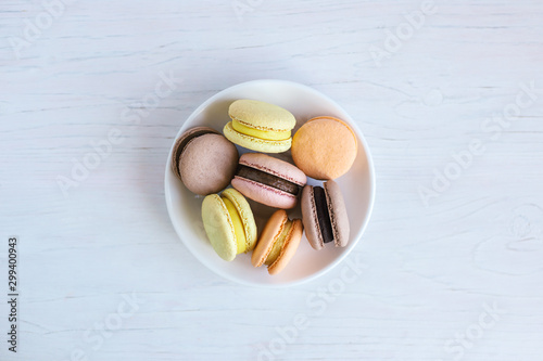 Tasty french macarons on a white plate.  White wooden background, flat lay.