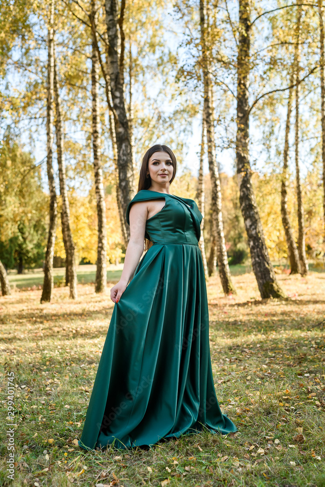 Naklejka premium Young woman wearing fashionable green dress walking in autumn park.