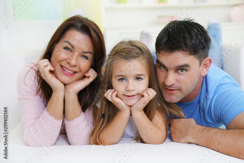 Happy young couple and daughter lying on bed ,looking at camera    