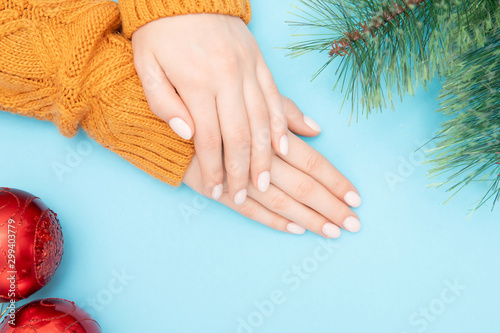 Female beautiful hands with manicure on nails in warm sweater with red Christmas ball new year on blue background. Top view