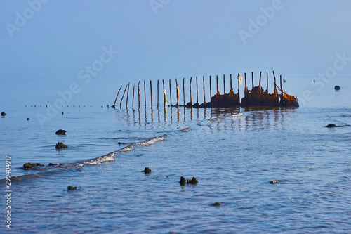 Old rusty breakwaters with ragged scraps of rope. Against the background of the sea merging with the sky. © OneBit