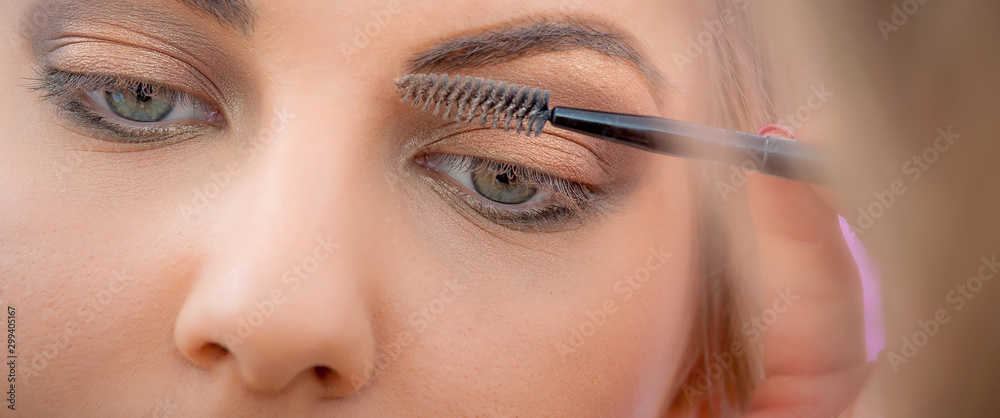 Makeup professional artist applying mascara on lashes of model eye