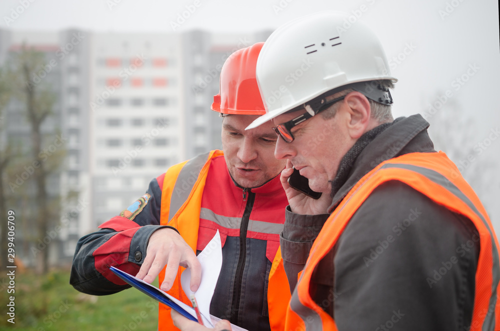 Obraz premium An engineer with a hard hat and helmet discussing a project at a construction site with a team leader in autumn or winter. architecture construction concept. Industrial safety