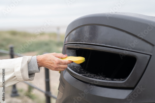 Person putting a banana peel in public outdoor trash can