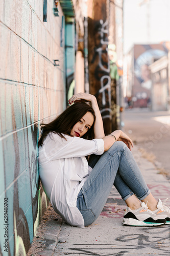 Pretty girl in white shirt, blue jeans with red lips. Posing in street. Sitting on the floor. Long hair. Bubble gum. Sunny day. Art district. Skinny girl modeling. Pretty woman, fashion girl.