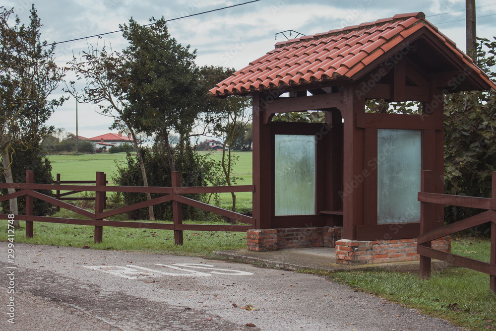 Wooden bus station in the village. Empty rural bus station along road with fence and trees. Travel and destination concept. Transportation concept. Countryside voyage. Journey background. Wooden bus station in the village. Empty rural bus station along road with fence and trees. Travel and destination concept. Transportation concept. Countryside voyage. Journey background.
