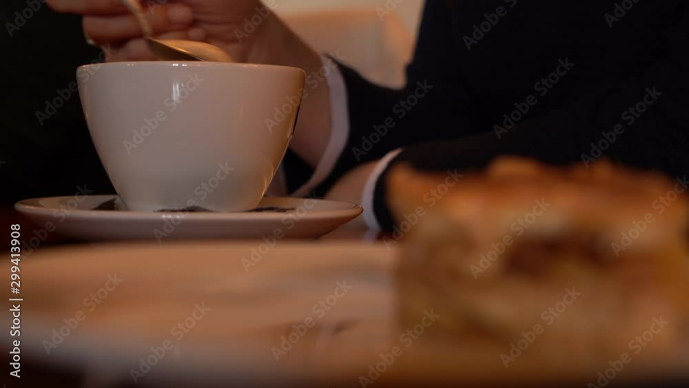 Close up shot of a person stirring a cup of coffee, a piece of cake on foreground Close up shot of a person stirring a cup of coffee, a piece of cake on foreground