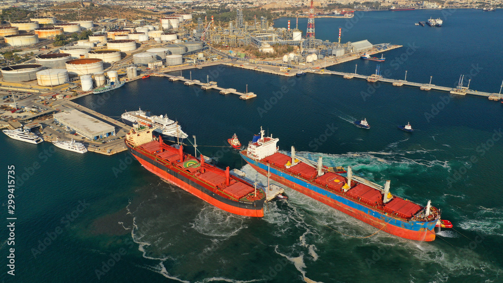 Obraz premium Aerial drone photo of industrial bulk carrier tanker being towed by tugboats in bay and shipyard of Elefsina, Attica, Greece