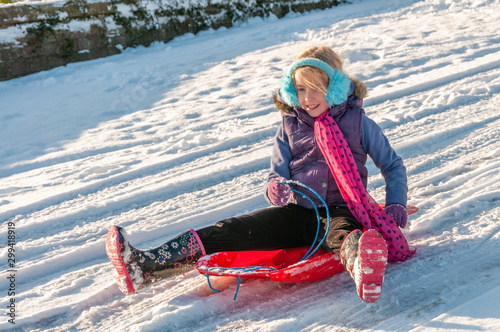 Happy young vibrantly dressed girl sledging with blue ear muffs photo