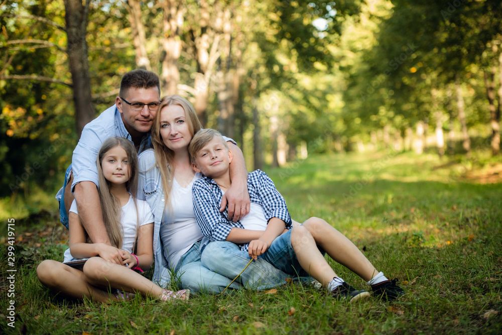 Happy family of four sitting on a grass in summer park outdoors and smiling