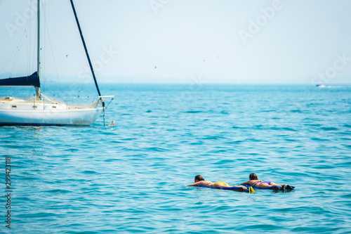 Garda, Italy - July, 06, 2019: image of vacationers floating on air mattresses near parked motor boats