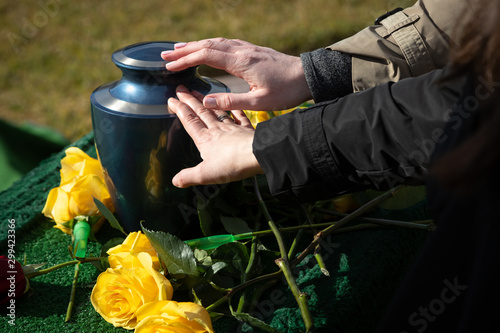 Two hands touching a cremation urn at a funeral