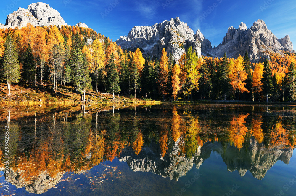 Lake with reflection of mountains at sunrise in autumn in Dolomites, Italy. Landscape with Antorno lake, blue fog over the water, trees with orange leaves and high rocks in fall. Colorful forest