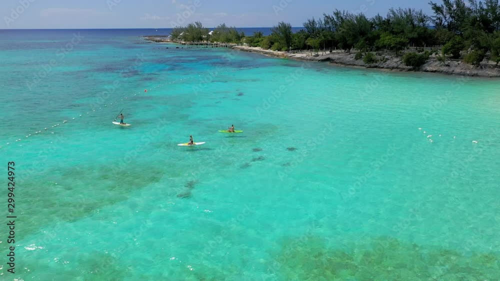 Aerial: Three Paddle Boarders in Clear Shallow Water Next to Deserted Island - Nassau, Bahamas Aerial: Three Paddle Boarders in Clear Shallow Water Next to Deserted Island - Nassau, Bahamas