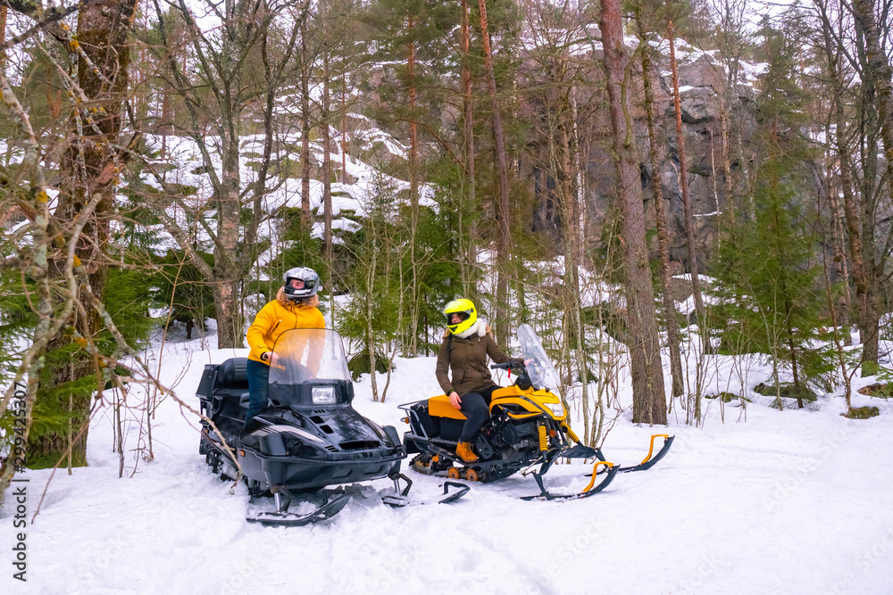 Snowmobiling. Guy and a girl travels through the forest. Riding through the coniferous forest. Lifestyle. A young couple on a snowmobile. Concept - snowmobile rides. Active winter holidays.