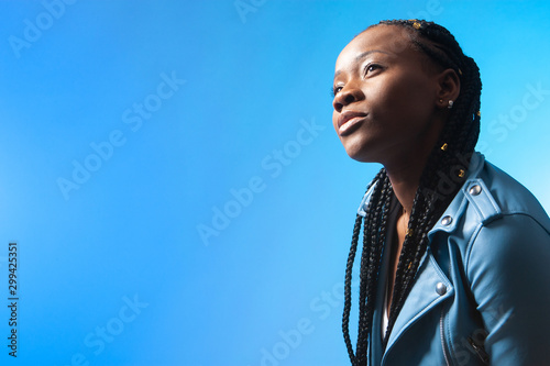 Girl is dreaming. African model. Woman is looking up. Dark-skinned girl on a blue background. Female student with african pigtails. Dreadlocks. African American thinks about the future