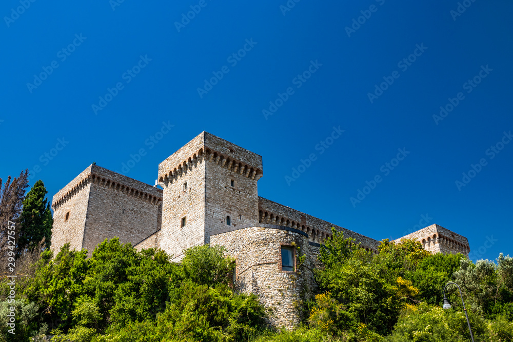The medieval castle of the ancient village of Narni. Umbria, Terni, Italy. The blue sky in summer. The stone walls and towers of the fortress. Green trees, vegetation, nature.