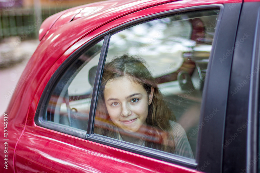 Young teenager girl in a red car looks out the window