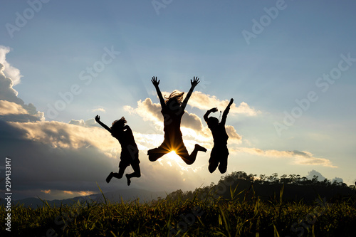 Silhouette group of happy children jumping playing on mountain at sunset, summer time