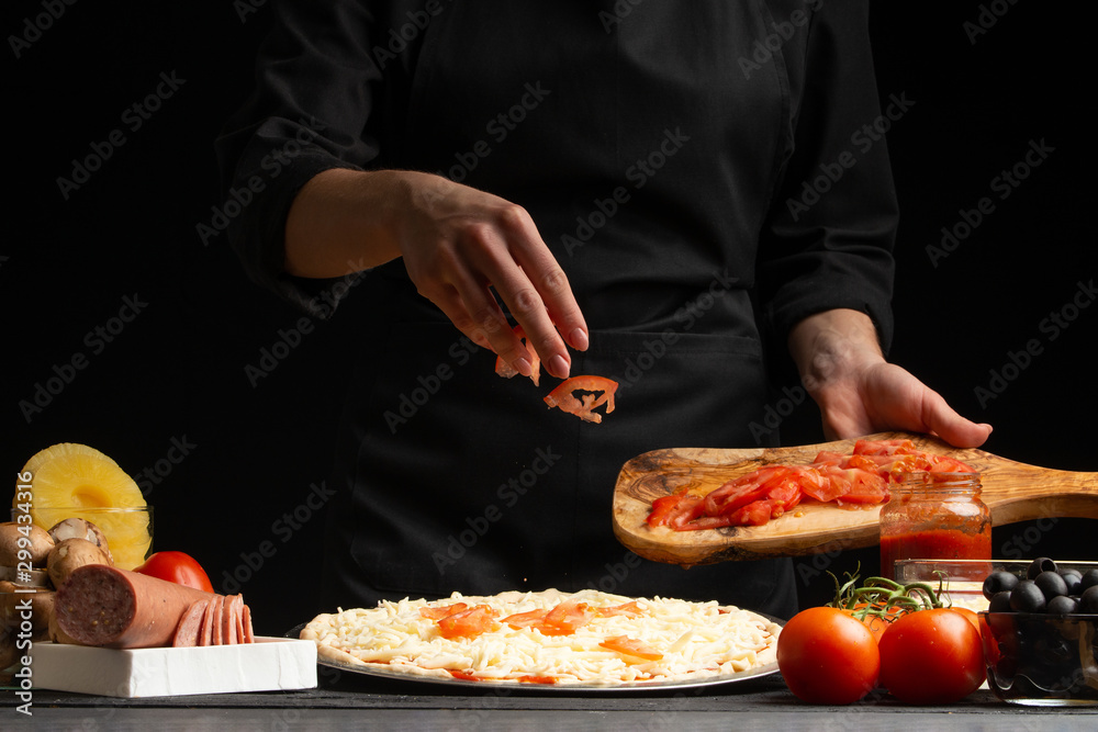 The chef cooks pizza, sprinkles fresh tomatoes, on a background with ingredients. Recipe book, menu, home cooking.