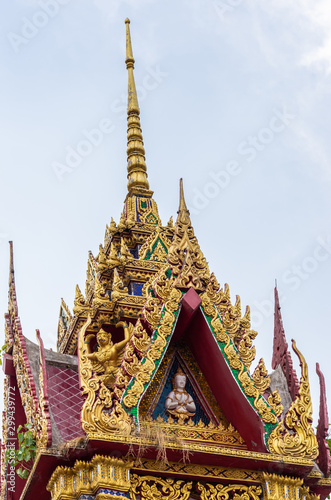 Ko Samui Island, Thailand - March 18, 2019: Wat Laem Suwannaram Chinese Buddhist Temple. Tower and spire of small golden shrine with statue, loudspeaker, blues and green foliage against silver sky.  photo