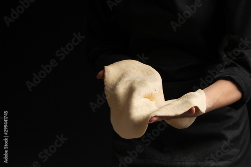 Chef pizza maker preparing pizza, holding rolled dough in hands. On a black background for design