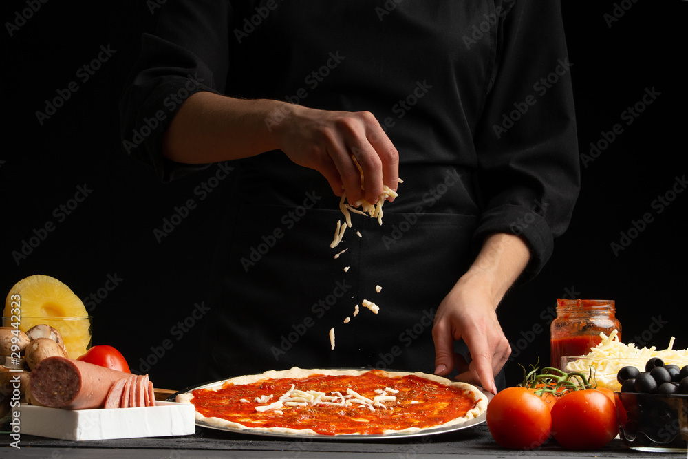 Chef cooks pizza, sprinkled with mozzarella cheese, freezing in motion on the background with ingredients. Recipe book, menu, home cooking