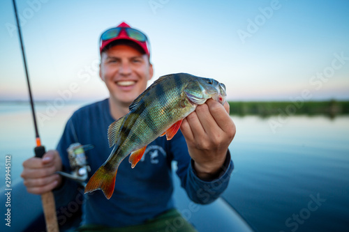 Cuadro en lienzo Happy amateur angler holds perch fish (Perca fluviatilis) in one hand and fishing rod in the other