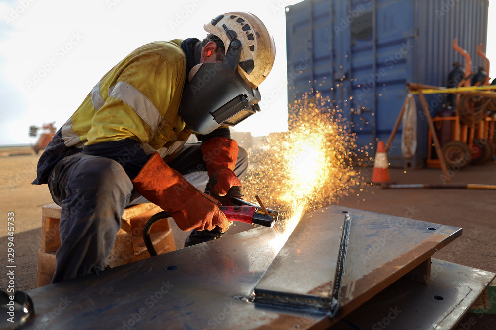 Construction worker wearing safety ears plug helmet, face shield, red welding leather glove protection while commencing hot work gouging metal plate on the ground surface Construction worker wearing safety ears plug helmet, face shield, red welding leather glove protection while commencing hot work gouging metal plate on the ground surface