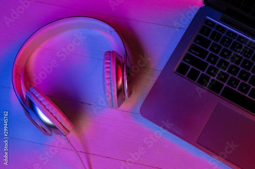 Top view of set of gadgets in purple neon light and pink background. Laptop keyboard, headphones and smartphone with black screen. Copyspace for your advertising. Tech, modern, gadgets. photo