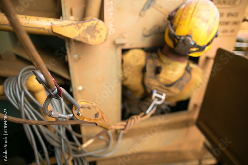Unfocused of rope access confined space worker wearing safety harness, helmet connecting three two one pulleys rescue system into back of his safety harness  loop prior entering into confined space  