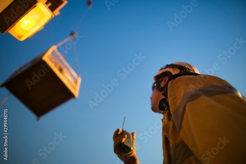 Defocused picture of rigger crane operator miner wearing helmet, using two way safety radio communicating with crane operator while load is being lift at construction mine site Perth, Australia  © Kings Access