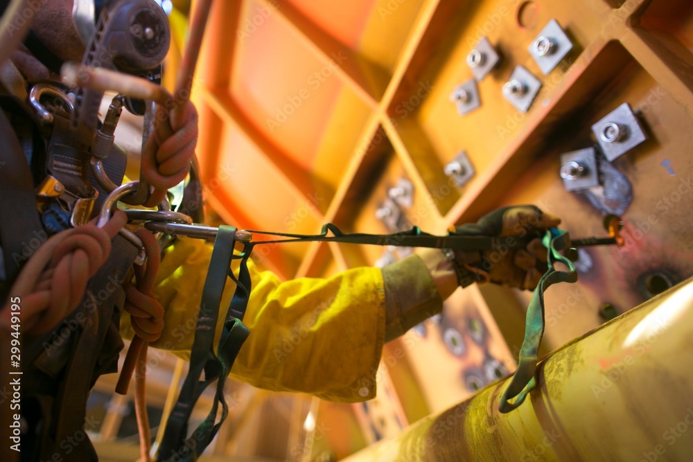Fototapeta premium Safe work practices rope access miner male hand working at heights commencing clipping positioning safety hook against the wall to stopping body swinging around while working on, construction site