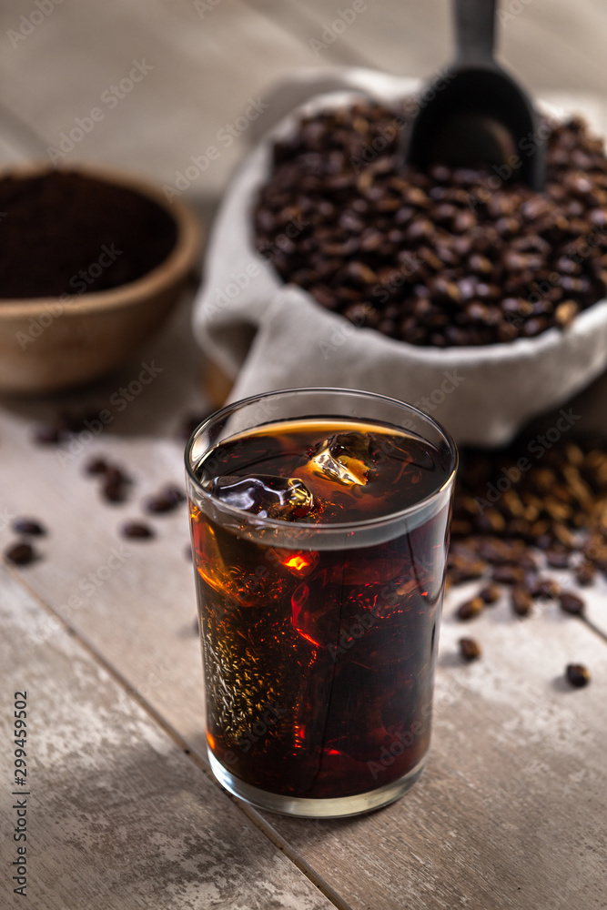 Glass of carbonated Ice coffee with ingredients, soda, whole roasted beans, scoop, grind, bag on wood Glass of carbonated Ice coffee with ingredients, soda, whole roasted beans, scoop, grind, bag on wood