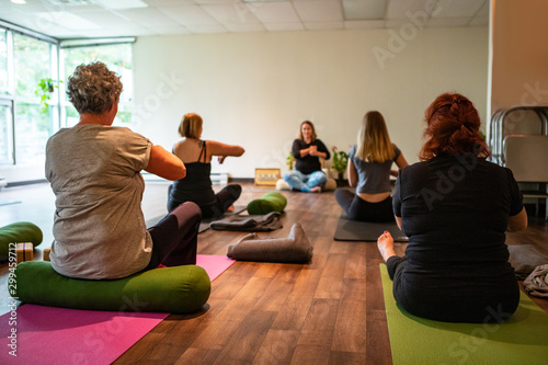 Backside view of an adult woman giving yoga instructions in a room full of people attending her class and following instructions photo