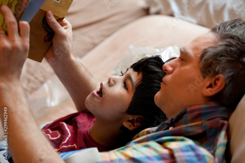  boy reading  book with father while lying in bed