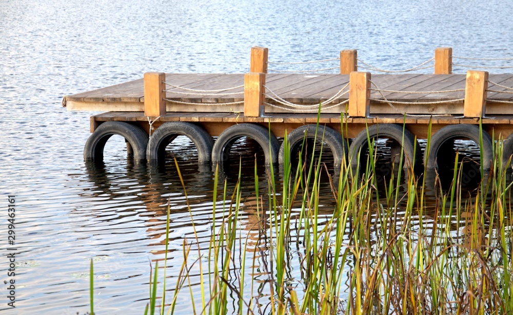 Obraz premium The pier on the river is new wooden. The pier is made of boards, logs, rope.