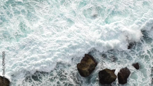 View of white ocean waves crashing into black rocky shore from above off of a cliff, Bali, Indonesia. Shot on Sony a6500 in 120fps. photo