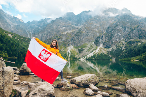 young pretty smiling woman holding poland flag at beach of mountain lake