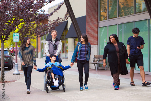 Disabled boy in wheelchair in city  with family and caregiver