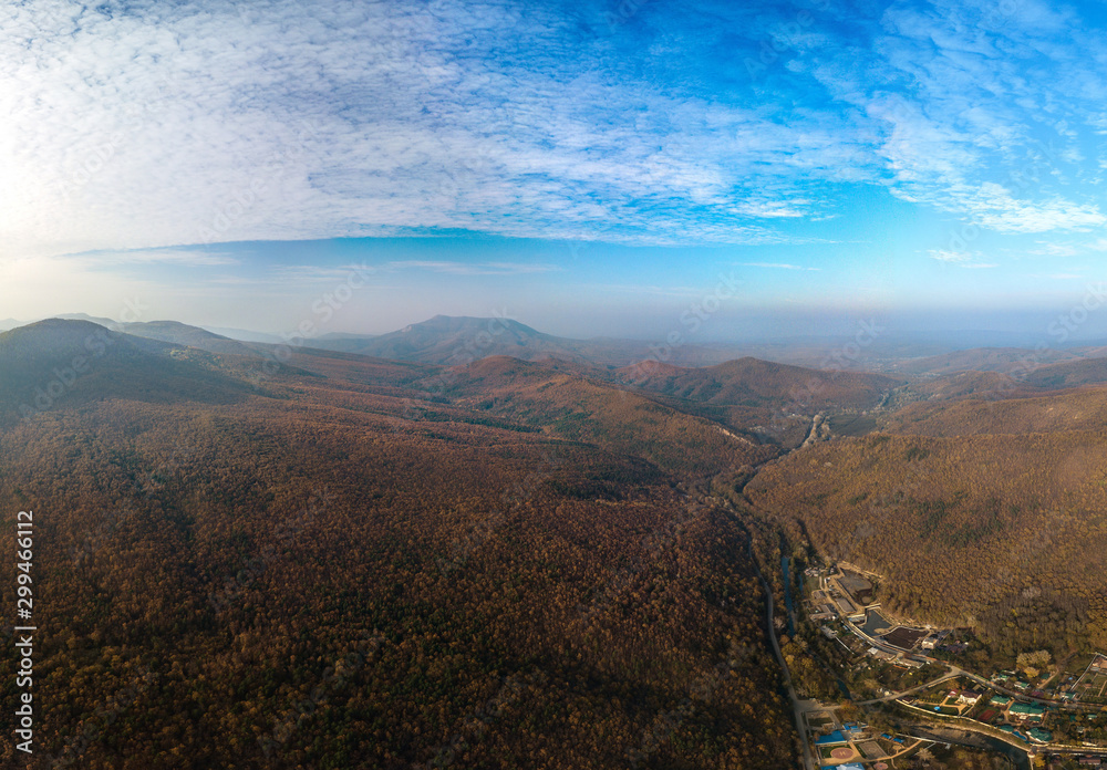 Autumn day with a slight haze on the horizon. Caucasus Mountains (Western Caucasus, South of Russia), covered with autumn yellow-brown forest. Aerial panorama over the Plancheskaya Shchel village 