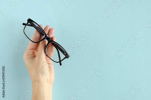 Hand with eyeglasses composition on blue background. photo