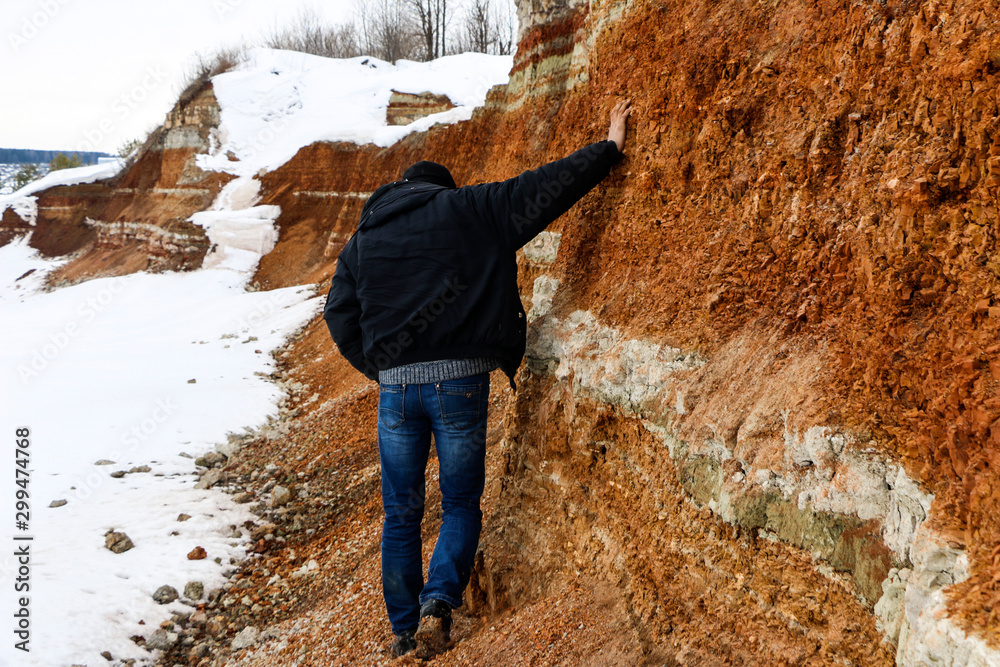 young man walks in  clay career in winter.  guy touches his hands with multi-colored layers of clay in  excavation.