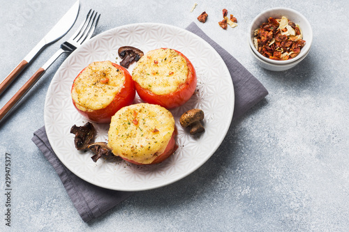 Baked whole tomatoes stuffed with mushrooms and cheese with spices on a light concrete background. Copy space.
