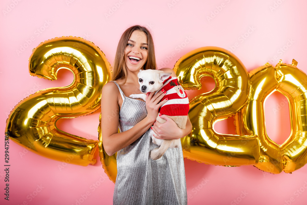 happy smiling woman with chihuahua white dog and 2020 christmas balloons isolated over pink