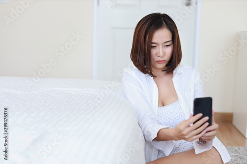 young attractive asian woman wearing white shirt using VDO call from cell phone and giving kiss in white bedroom