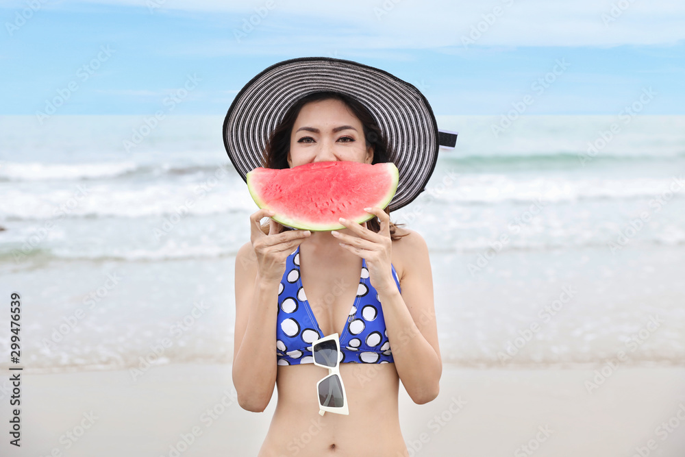 Stockfoto Asian girl short hairs and sexy body who wearing blue bikini and  nice hat. She holding and eating watermelon with a happy smiling face  during summer holidays on beautiful beach