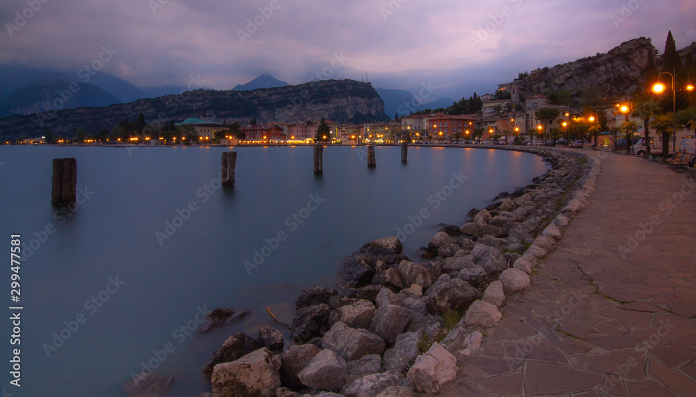 Obraz premium panoramic city lake view of torbole at blue hour; evening long term exposure of lake garda (lago di garda,italy)