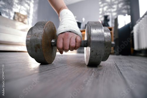 Wide angle photo of broken fractured hand in plaster cast holding dumbbell. Home trainig rehabilitaion after accident. photo